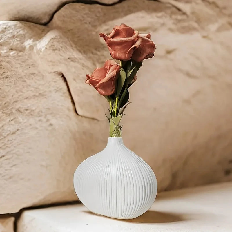 A vase of pink roses in a white ribbed ceramic vase set against a textured stone background.