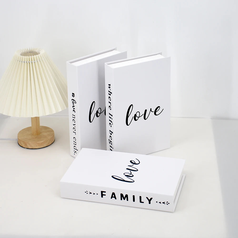 A set of three modern decorative fake books in white, featuring the text love where life begins and love family.