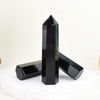 A black obsidian crystal obelisk point standing on a white surface.