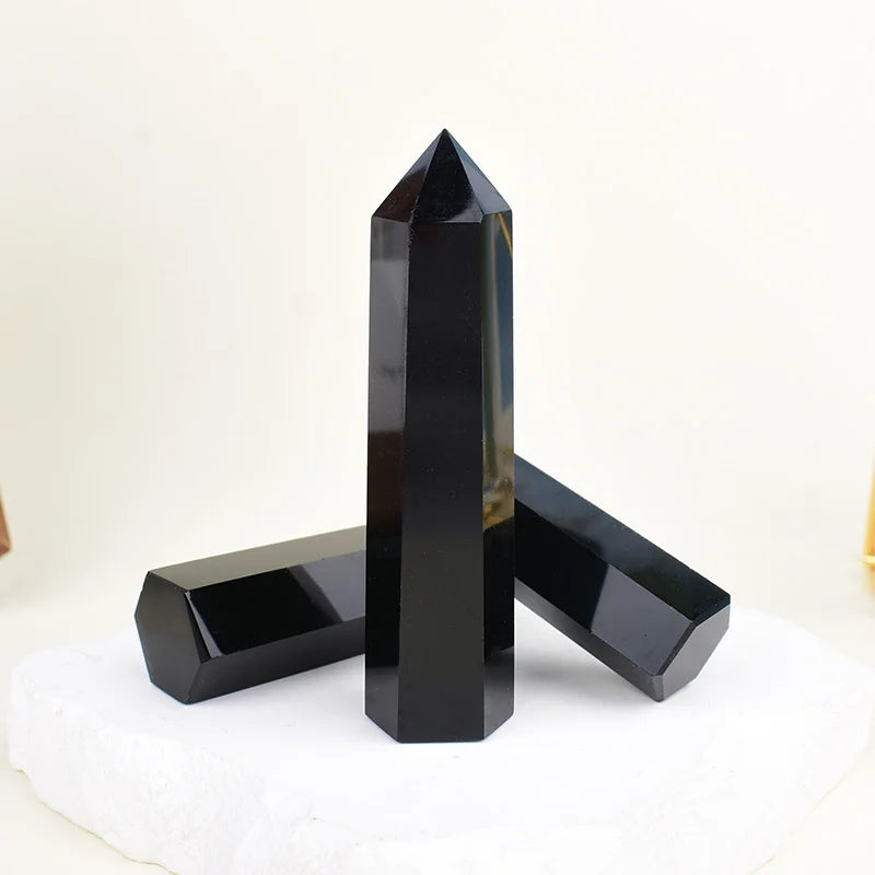 A black obsidian crystal obelisk point standing on a white surface.