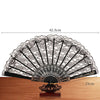 An elegant black and white lace folding hand fan displayed on a wooden surface.