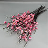 A cluster of pink artificial plum blossoms on dark branches.