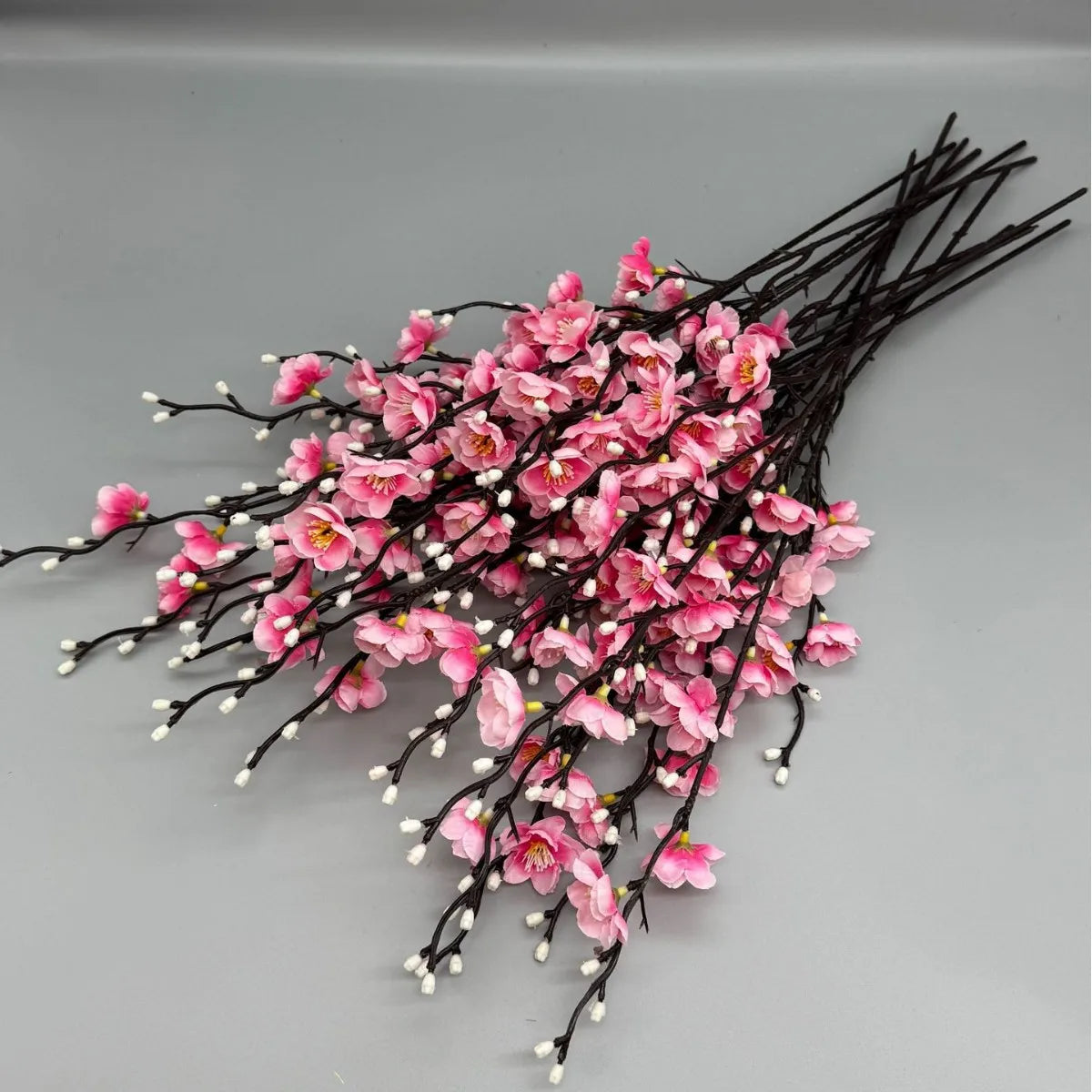 A cluster of pink artificial plum blossoms on dark branches.