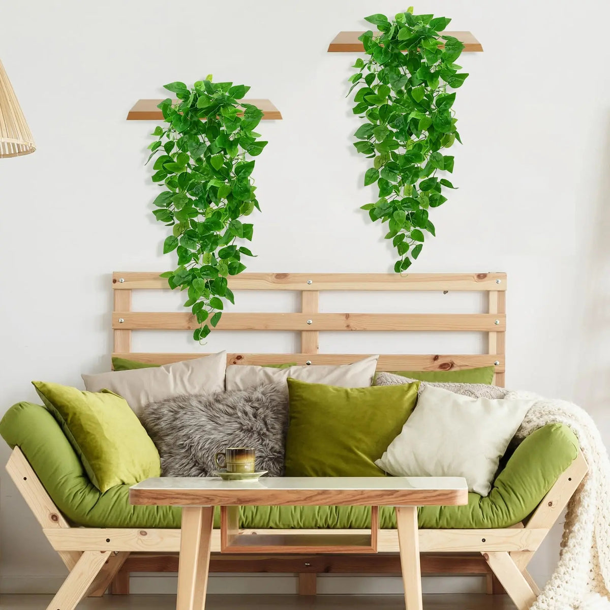 Artificial pothos hanging vines used as wall decor above a wooden bed frame with green and beige pillows