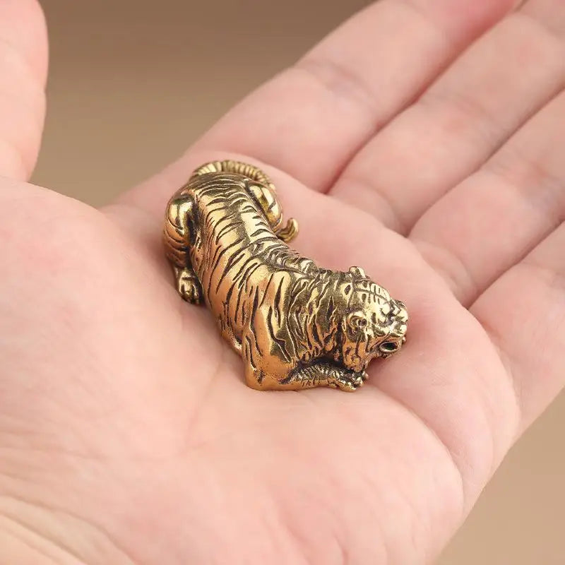 A vintage brass tiger figurine, a miniature animal statue, is held in a person's hand.