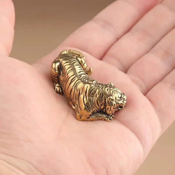 A vintage brass tiger figurine, a miniature animal statue, is held in a person's hand.