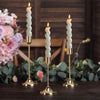 A set of twelve elegant gold metal candle holders with white candles displayed on a dark wooden surface.