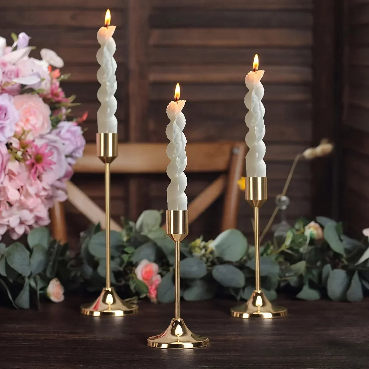 A set of twelve elegant gold metal candle holders with white candles displayed on a dark wooden surface.