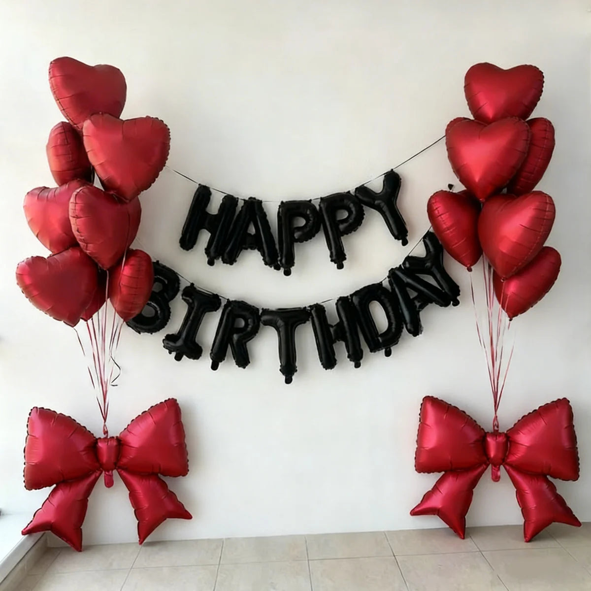 A decorative banner made of black heart balloons spelling out HAPPY BIRTHDAY with red balloons and bow accents.