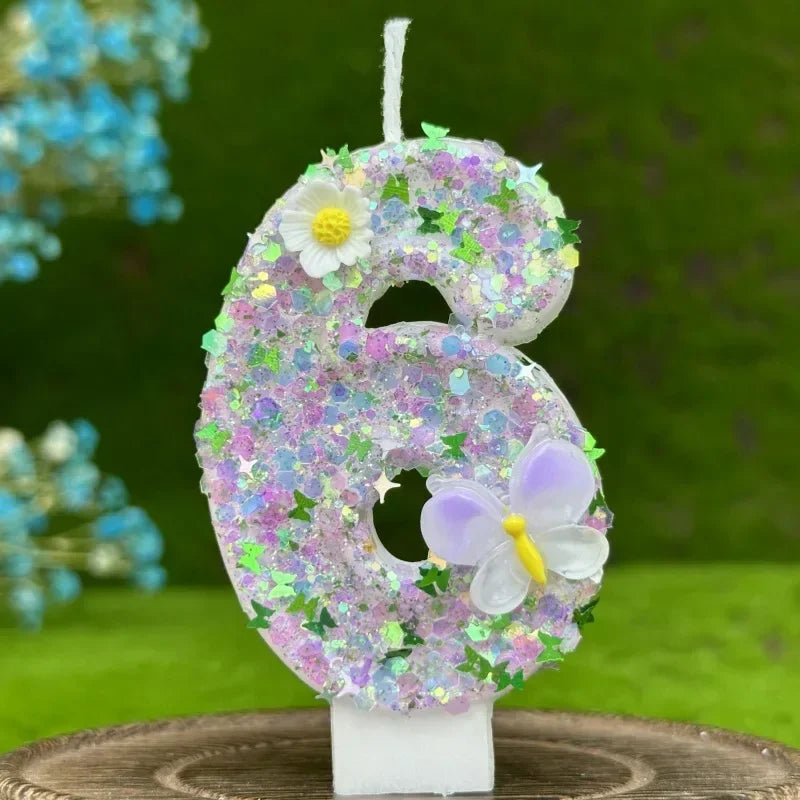 A large number six cake decorated with purple and pink glitter, featuring a white flower and a translucent purple butterfly.