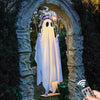 A white glowing ghost decoration is hanging inside an arched stone entryway surrounded by dark greenery.