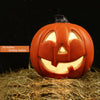 Linterna de calabaza de cerámica naranja tallada con cara sonriente sobre paja.
