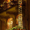 A vertical string of warm yellow Christmas lights shaped like a ladder, with an orange Santa figure at the top, decorating a 