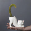 A white ceramic cat planter with a green succulent plant shaped like a curved tail is held in a hand.