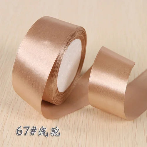 A roll of satin ribbon in a nude or champagne color is shown on a wooden surface.