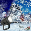 A black USB rotating LED snowflake projection light illuminates a snowy outdoor scene with falling snowflakes and a deer.