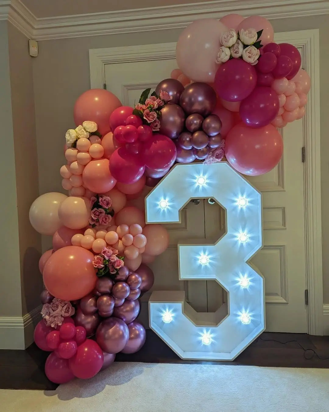 A large balloon garland in shades of pink and purple forms the number 3 for a celebration.