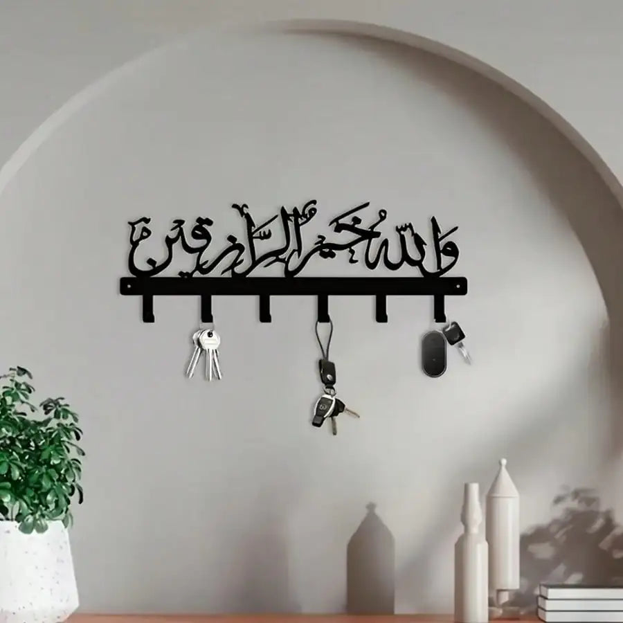 A black Islamic Arabic blessing key holder with hooks mounted on a light gray wall.