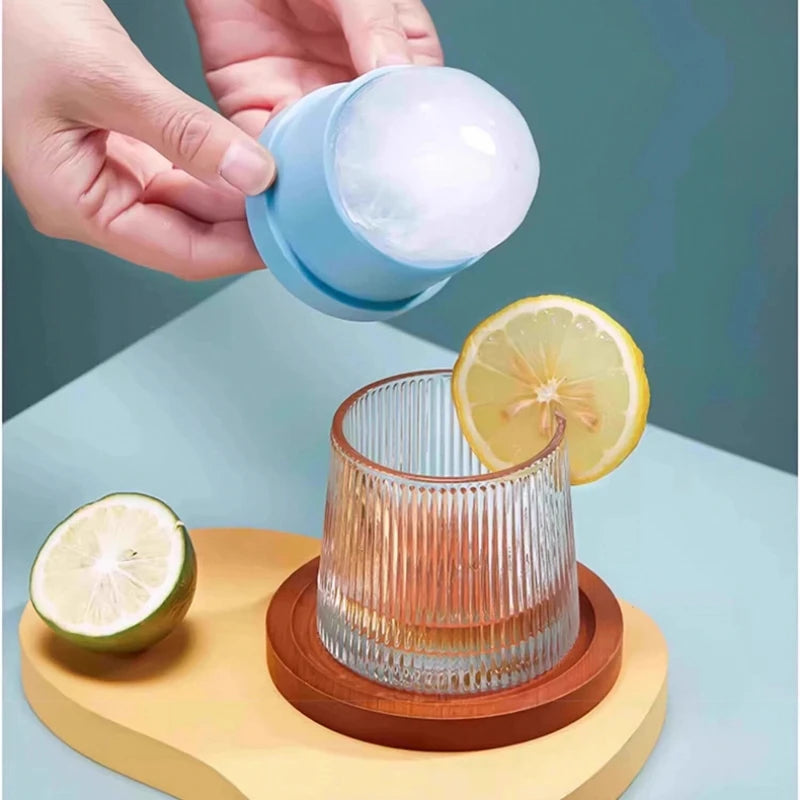 A hand holds a blue spherical ice mold over a glass of liquid, with a lime half nearby.