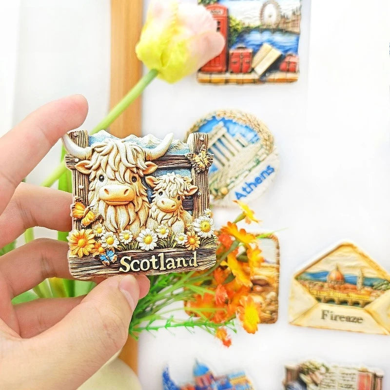A hand holds a Scottish Highland Cow fridge magnet featuring a 3D shaggy cow with a calf, set against a white background.