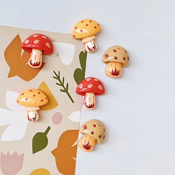 A set of nine cute decorative mushroom fridge magnets in various colors and styles against a light background.