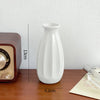 A white ceramic bud vase is shown next to a wooden box and a piece of paper on a brown table.