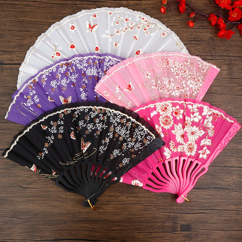 A collection of five elegant plum blossom folding fans in white, purple, pink, and black resting on a dark wooden surface.