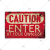 A vintage red metal warning sign with yellow text that reads CAUTION ENTER AT YOUR OWN RISK.