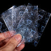 A hand holds several holographic card sleeves, clear protectors for trading cards and photos.