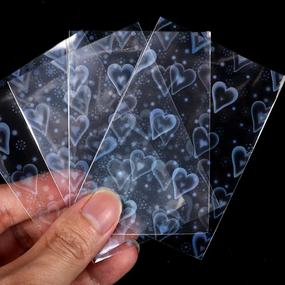 A hand holds several holographic card sleeves, clear protectors for trading cards and photos.