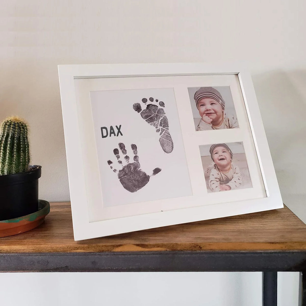 A white photo frame displaying a baby's handprint and footprint, alongside a portrait of the baby.