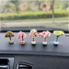 Five miniature tree ornaments with pink and green flowers displayed on a car dashboard.