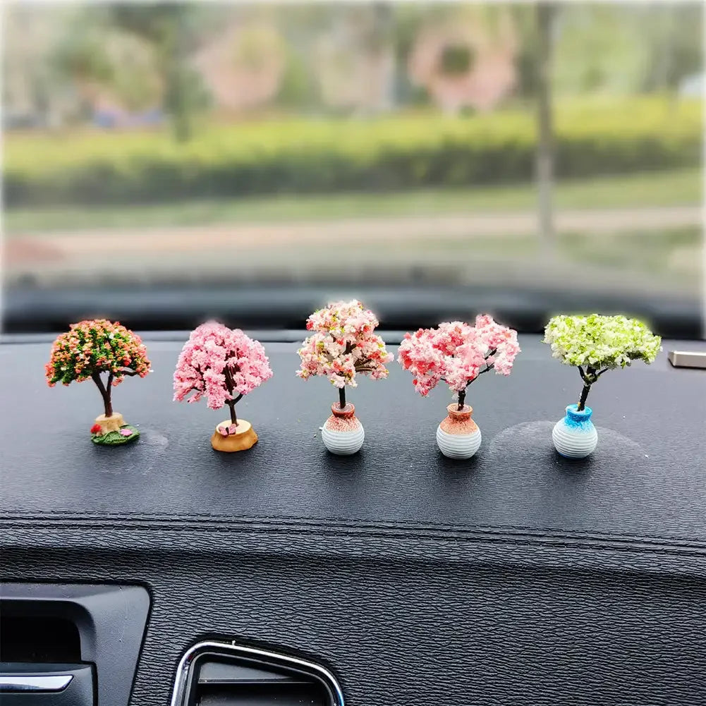 Five miniature tree ornaments with pink and green flowers displayed on a car dashboard.