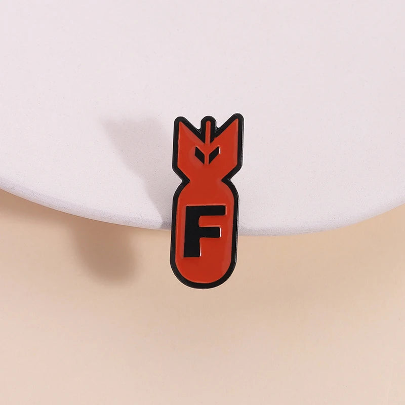 An orange enamel pin shaped like an explosive shark head with the letter F inside.
