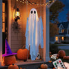 A white ghost decoration hangs from a wire against a wooden wall with string lights and pumpkins in the background.