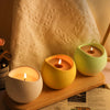 A collection of yellow and green silicone arc candle jars resting on a wooden surface next to a white textured fabric.