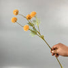 Una mano sostiene un tallo con crisantemos artificiales naranjas y hojas verdes para decorar.