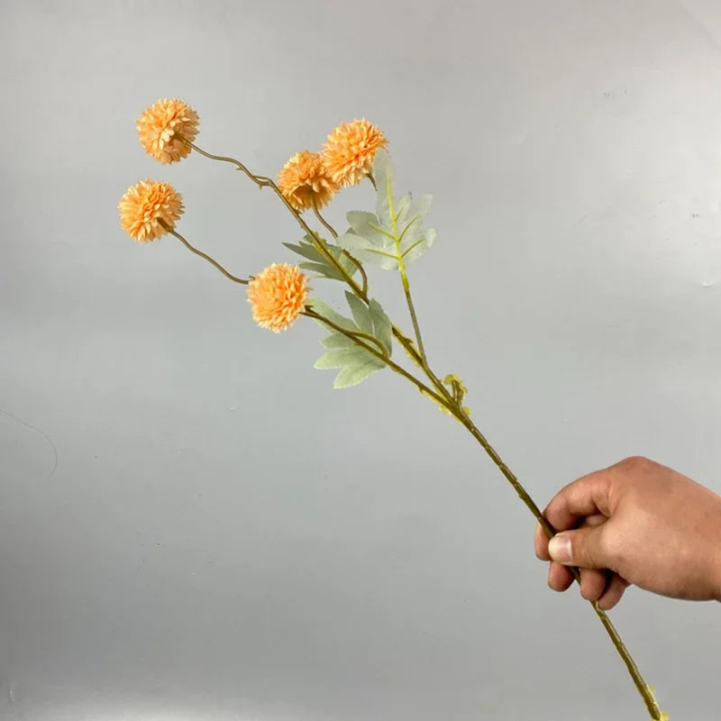 Una mano sostiene un tallo con crisantemos artificiales naranjas y hojas verdes para decorar.