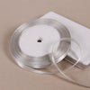 A roll of silver satin ribbon on a white spool resting on a light-colored surface.