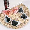 A collection of heart-shaped party sunglasses in pink and silver are displayed on a woven mat.