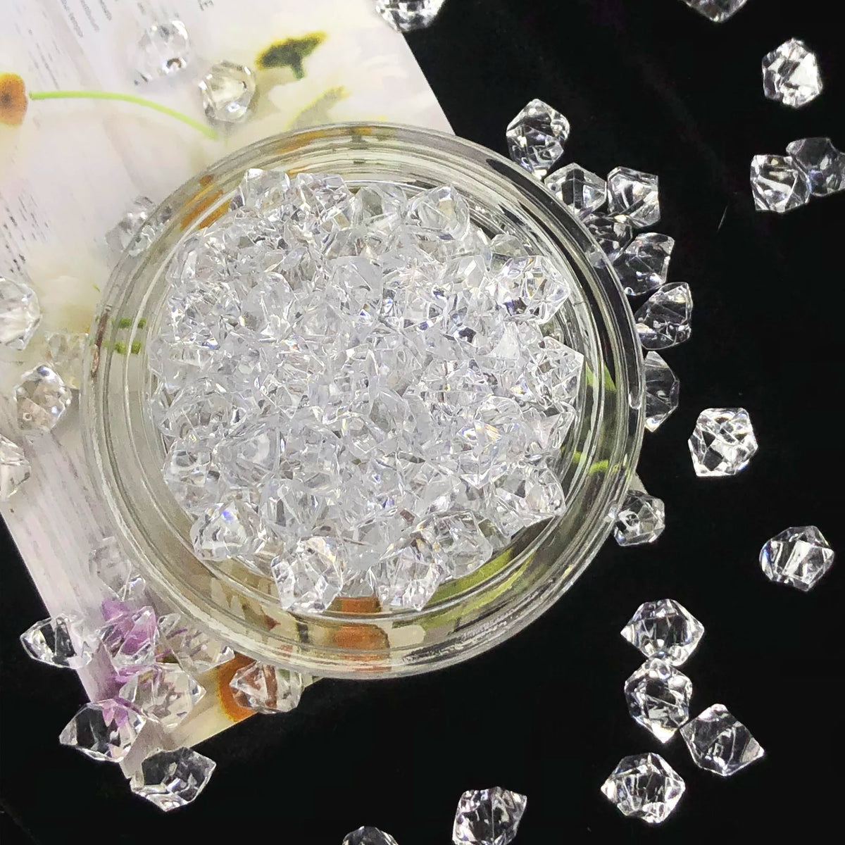 A clear glass jar filled with crystal ice cubes surrounded by loose acrylic stones and small clear crystals.