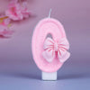 Glittery pink number 0 birthday candle with a decorative pink bow on a white base