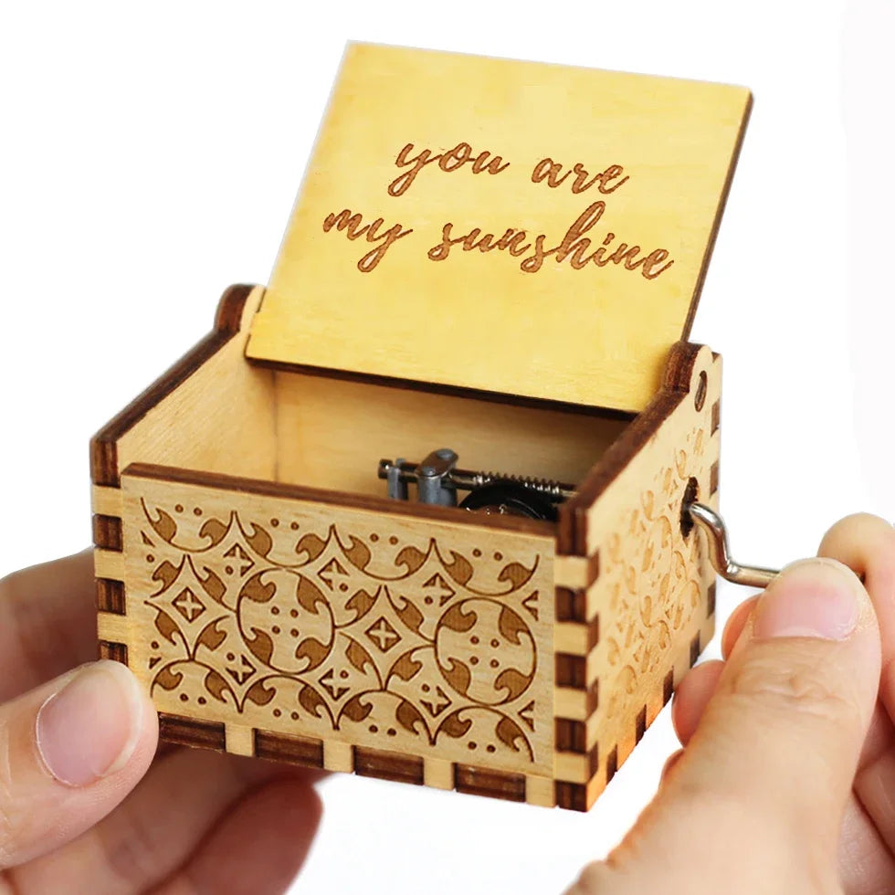 A carved wooden music box with a lid showing the message you are my sunshine being held in a hand