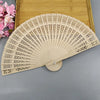 A light beige wooden folding hand fan with intricate cutouts is displayed on a wooden tray.