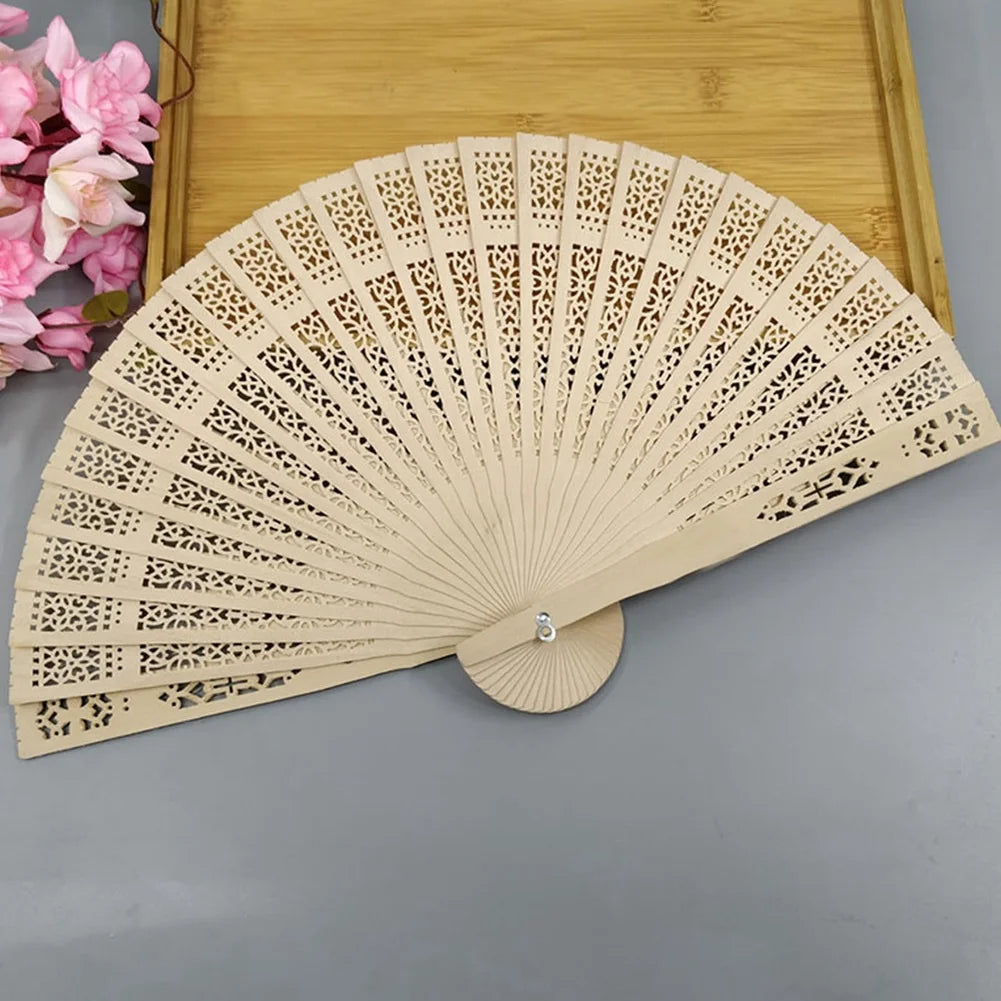 A light beige wooden folding hand fan with intricate cutouts is displayed on a wooden tray.