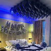 Bett dekoriert mit dunkelblauen Ballons und einem silbernen Briefballonbanner in einem schwach beleuchteten Raum.