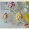 A bouquet of artisan tulips in pink and yellow are displayed with wax candles on a white surface.