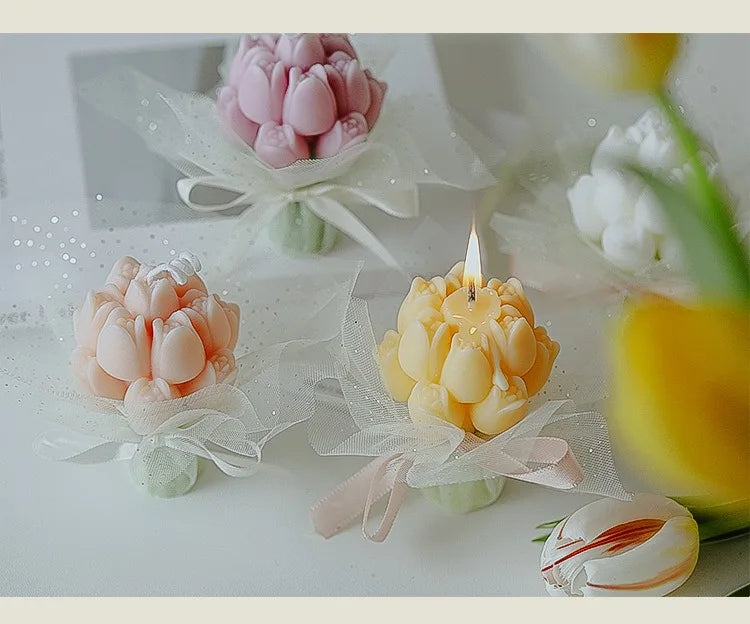 A bouquet of artisan tulips in pink and yellow are displayed with wax candles on a white surface.