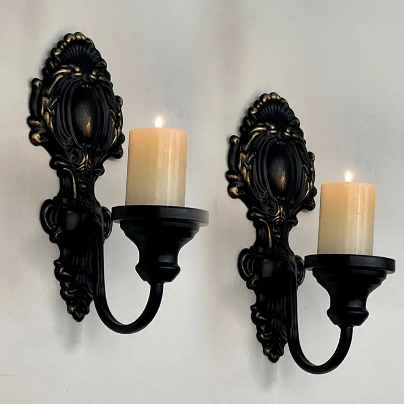 A set of two vintage wrought iron wall-mounted candle holders with cream-colored candles.