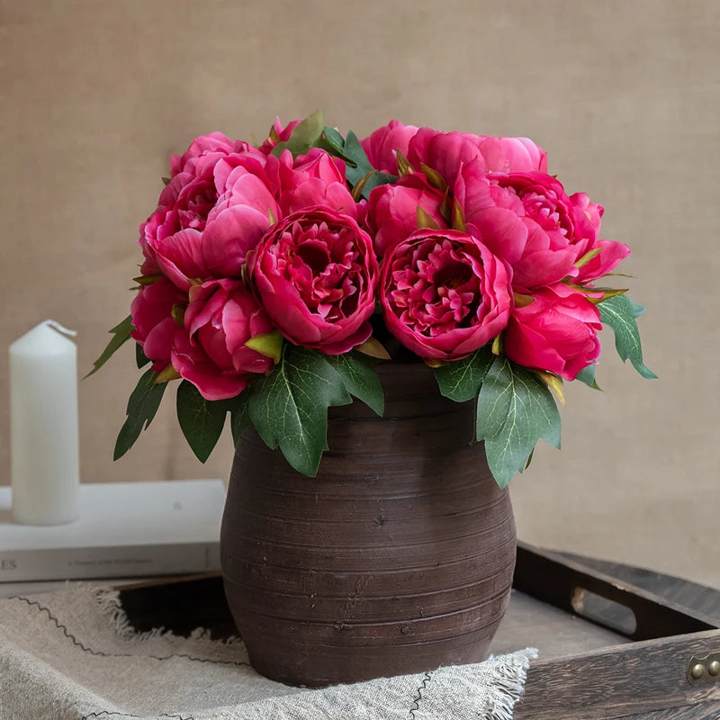 A bouquet of vibrant pink and magenta artificial silk peonies in a dark brown ceramic vase.